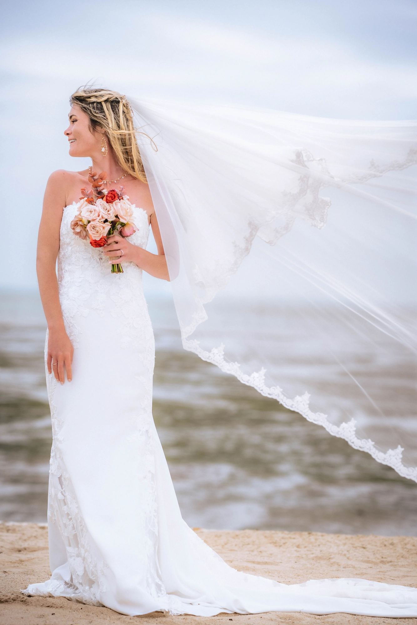 Mariée seule sur la plage, voile flottant dans le vent