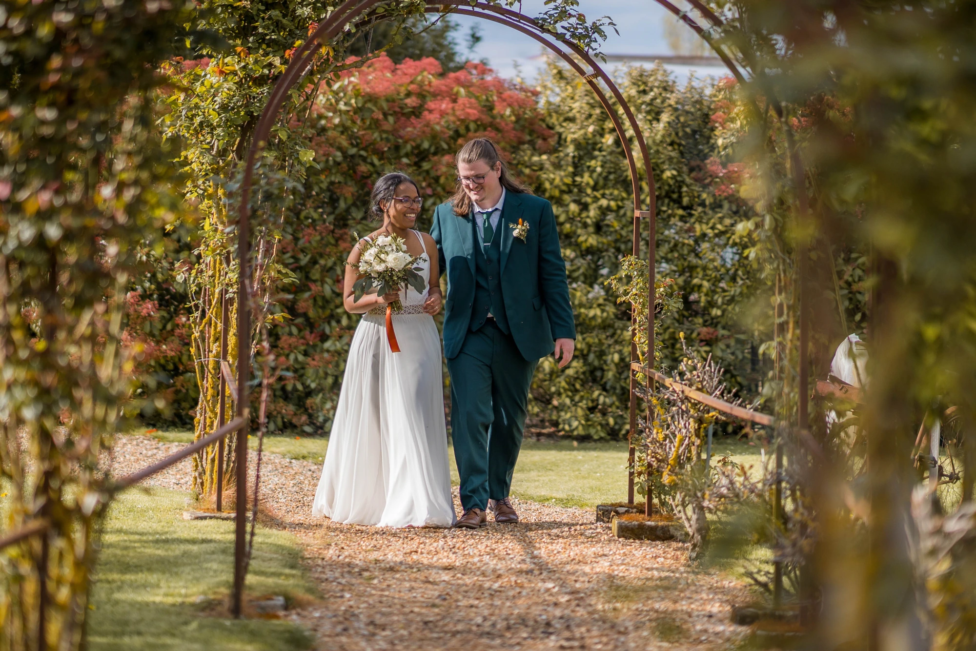 Mariée et marié marchant sous une arche de fleurs