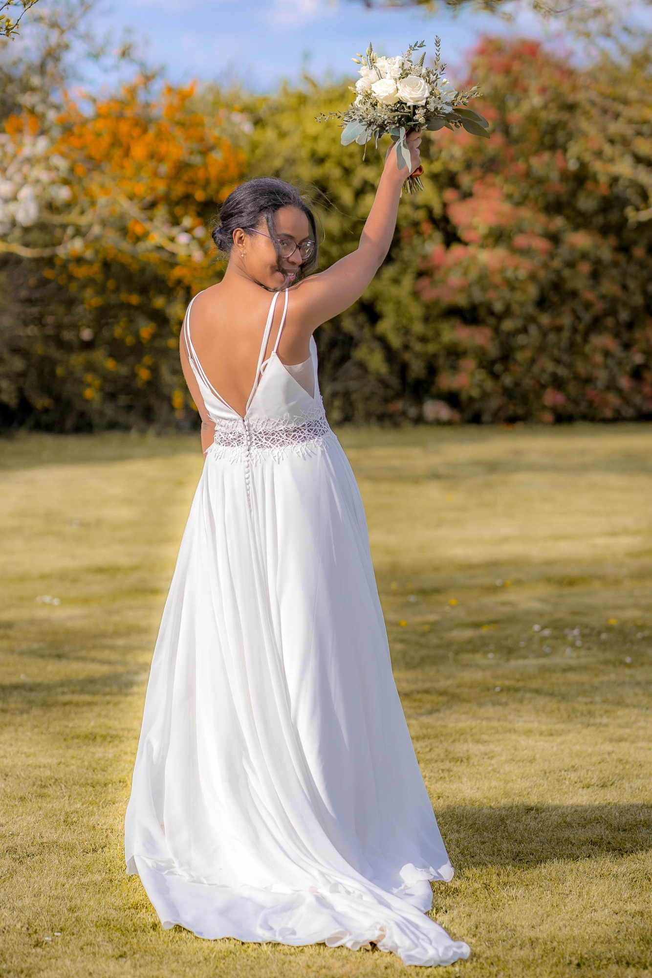Mariée dans un champ, de dos, bouquet levé